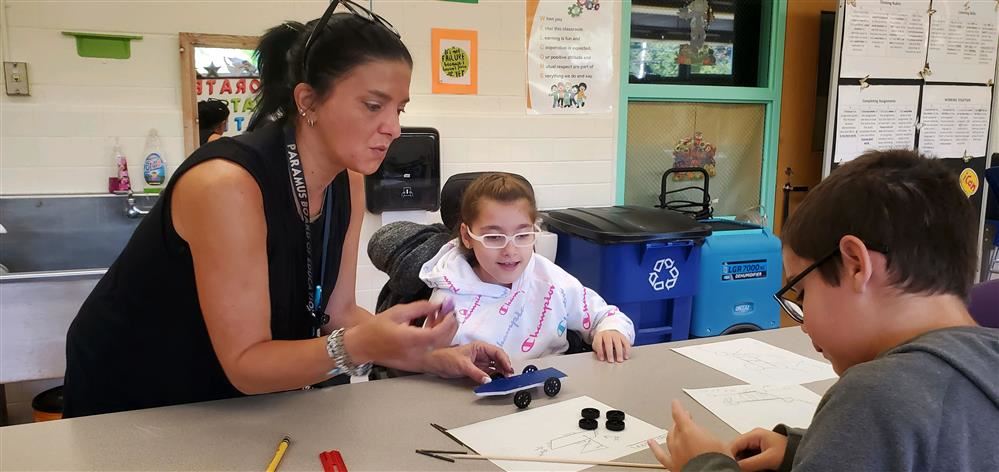  Students working together with an adult at a classroom table.